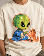 Close-up of a green alien touching paws with an orange kitten printed on an off-white oversized French terry t-shirt