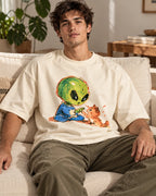 Man on a sofa in an off-white oversized French terry t-shirt with a green alien touching paws with an orange kitten
