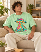 Man relaxing on a couch in the Tropical Transmission UFO oversized tee, jade