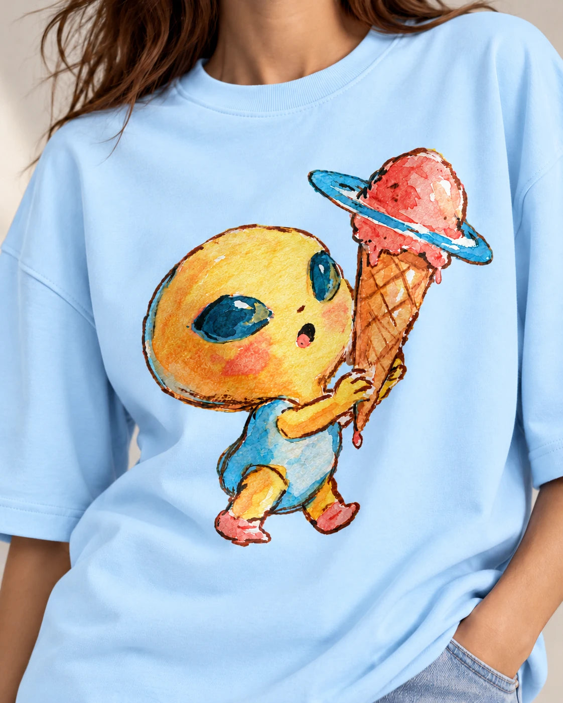 Close-up of a yellow alien holding a Saturn-ringed ice cream cone printed on a baby blue oversized French terry t-shirt