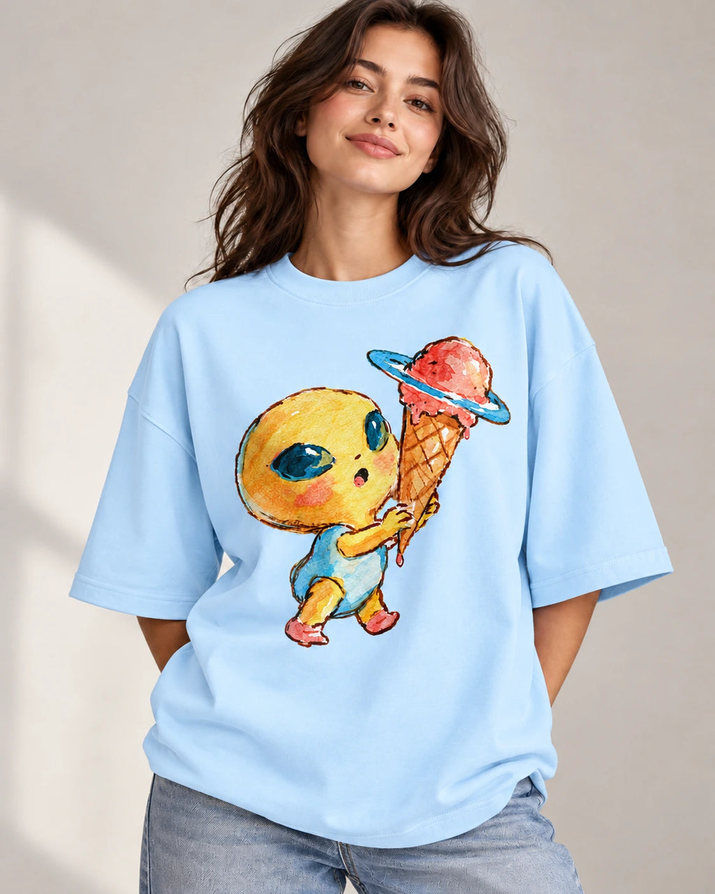 Woman in a baby blue oversized French terry t-shirt printed with a yellow alien holding a Saturn-ringed ice cream cone