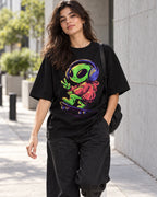 Woman on a street in a black oversized French terry t-shirt with a green alien in headphones skateboarding with a peace sign