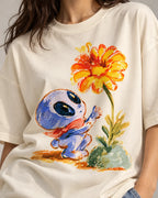 Close-up of a blue alien in a red scarf reaching for an orange flower printed on an off-white oversized French terry t-shirt