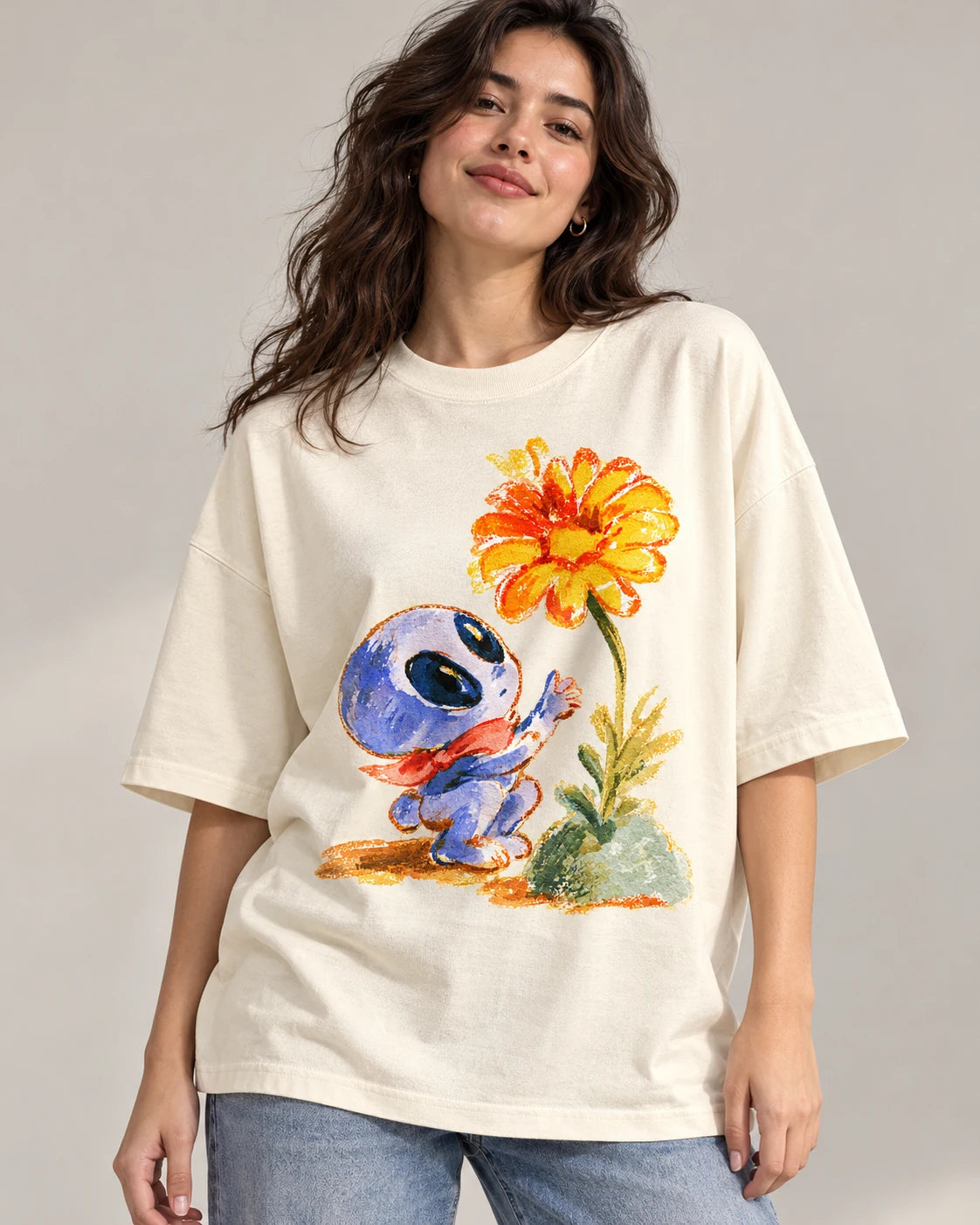 Woman in an off-white oversized French terry t-shirt printed with a blue alien in a red scarf reaching for an orange flower