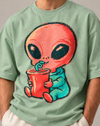 Close-up of a coral alien sipping a red cup through a curly straw printed on a jade oversized French terry t-shirt
