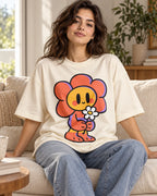 Woman on a sofa in an off-white oversized French terry t-shirt with a smiling orange flower character holding a daisy