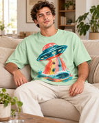 Man relaxing on a couch in the Tidal Transit UFO oversized tee, jade