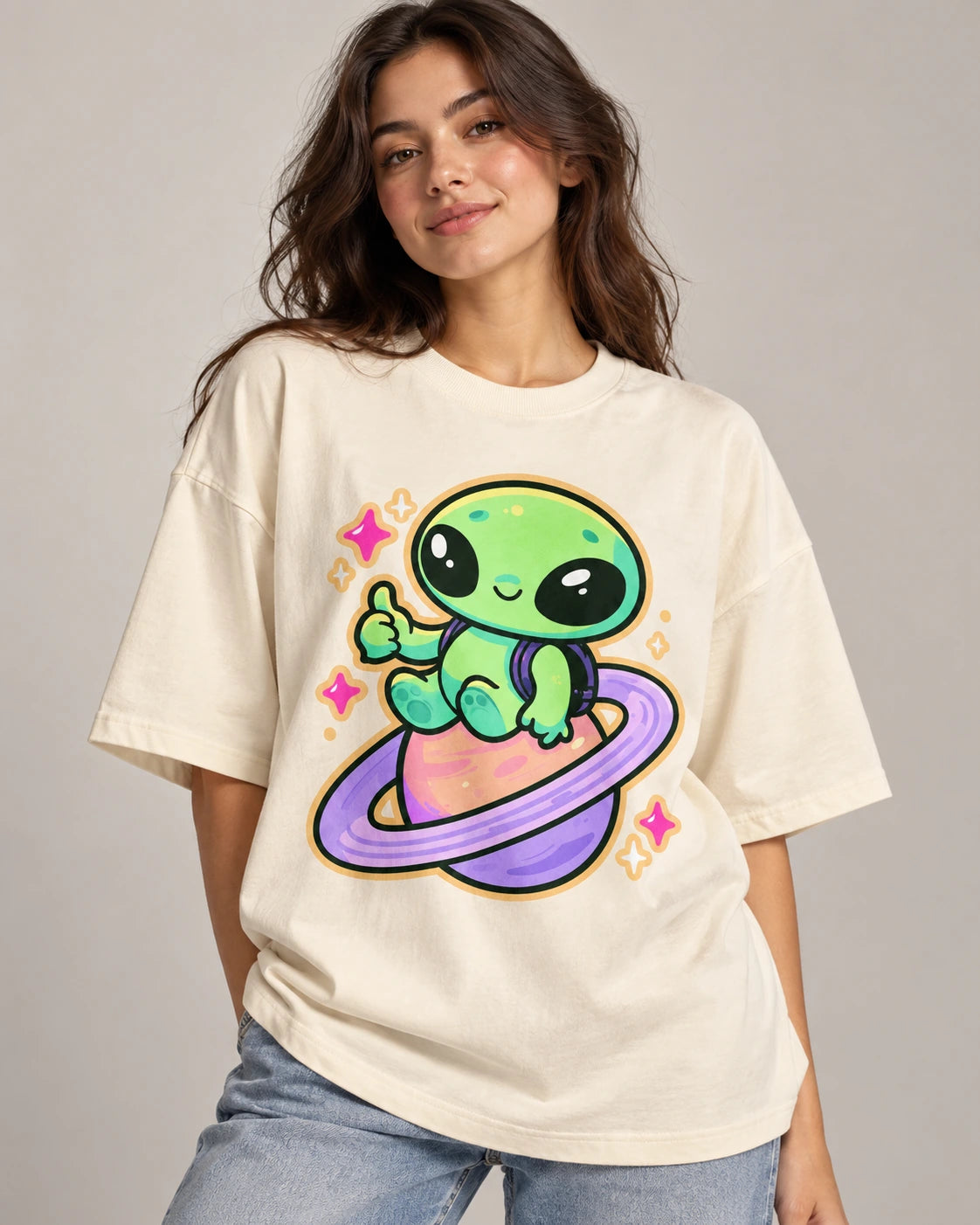Woman in an off-white oversized French terry t-shirt printed with a green alien giving a thumbs-up on a ringed planet