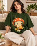 Woman on a sofa in a bottle green oversized French terry t-shirt with a mushroom sprite in a scarf holding a glowing spark