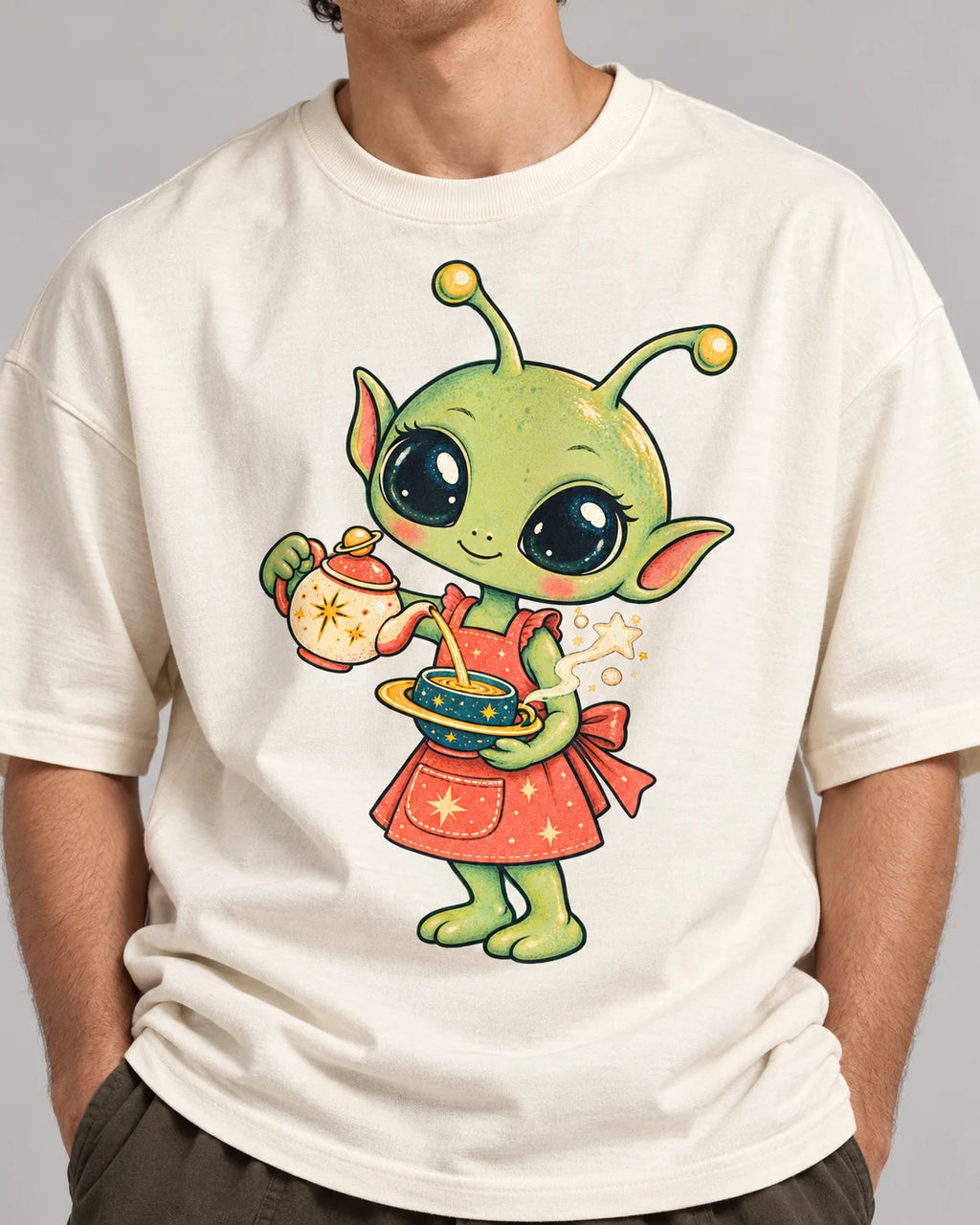 Close-up of a green alien in an apron pouring tea from a teapot printed on an off-white oversized French terry t-shirt