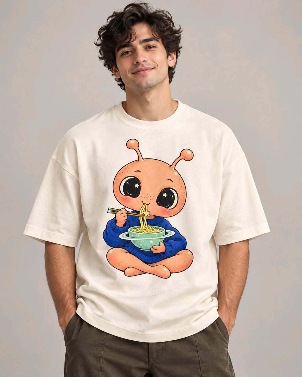 Man in an off-white oversized French terry t-shirt printed with a peach alien eating noodles from a ringed bowl
