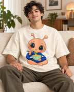 Man on a sofa in an off-white oversized French terry t-shirt with a peach alien eating noodles from a ringed bowl