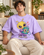 Man on a sofa in a lavender oversized French terry t-shirt with a yellow alien in a tracksuit holding a cassette player