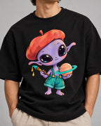 Close-up of a purple alien in a beret painting a ringed planet printed on a black oversized French terry t-shirt