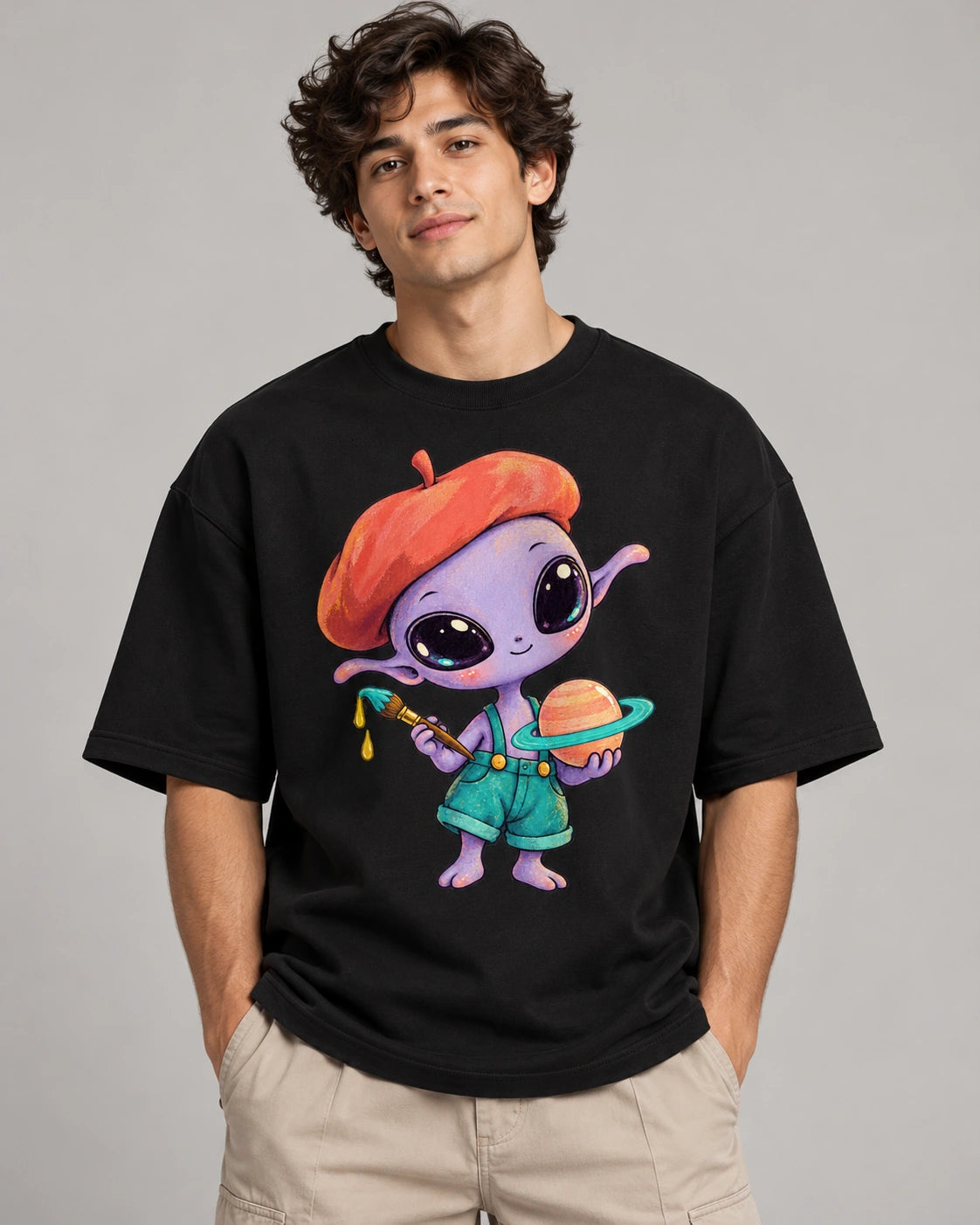 Man in a black oversized French terry t-shirt printed with a purple alien in a beret painting a ringed planet