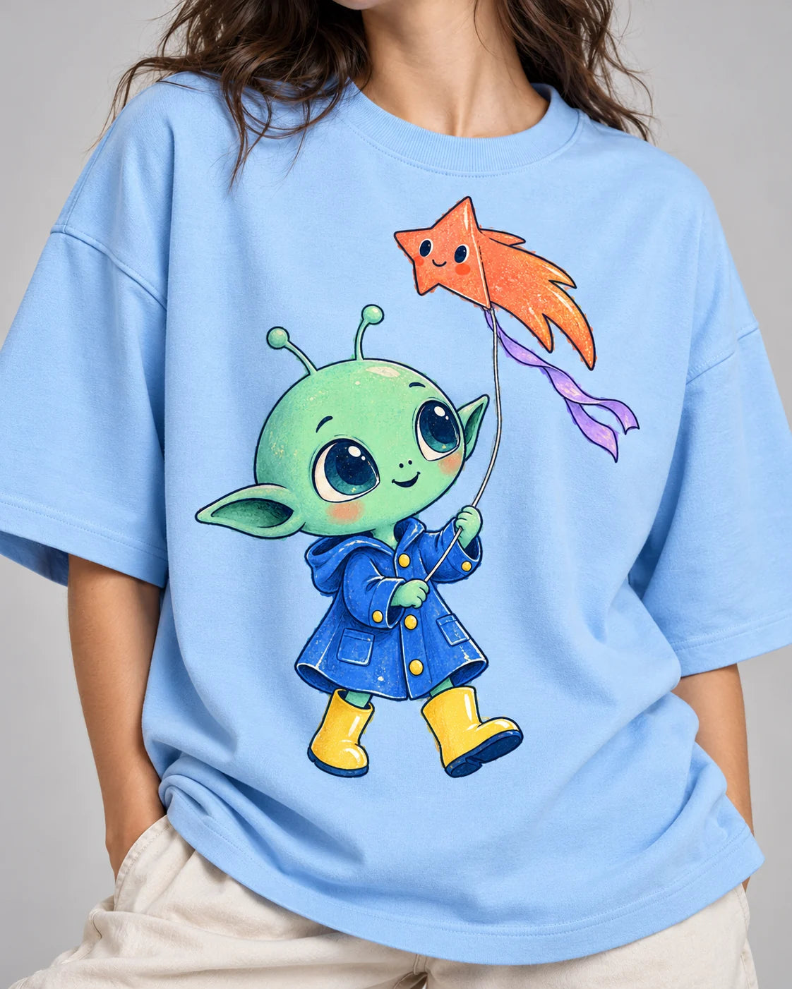 Close-up of a green alien in a raincoat flying a star-shaped kite printed on a baby blue oversized French terry t-shirt