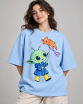 Woman in a baby blue oversized French terry t-shirt printed with a green alien in a raincoat flying a star-shaped kite