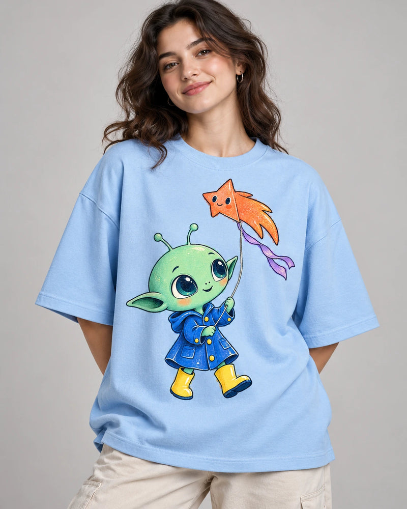 Woman in a baby blue oversized French terry t-shirt printed with a green alien in a raincoat flying a star-shaped kite
