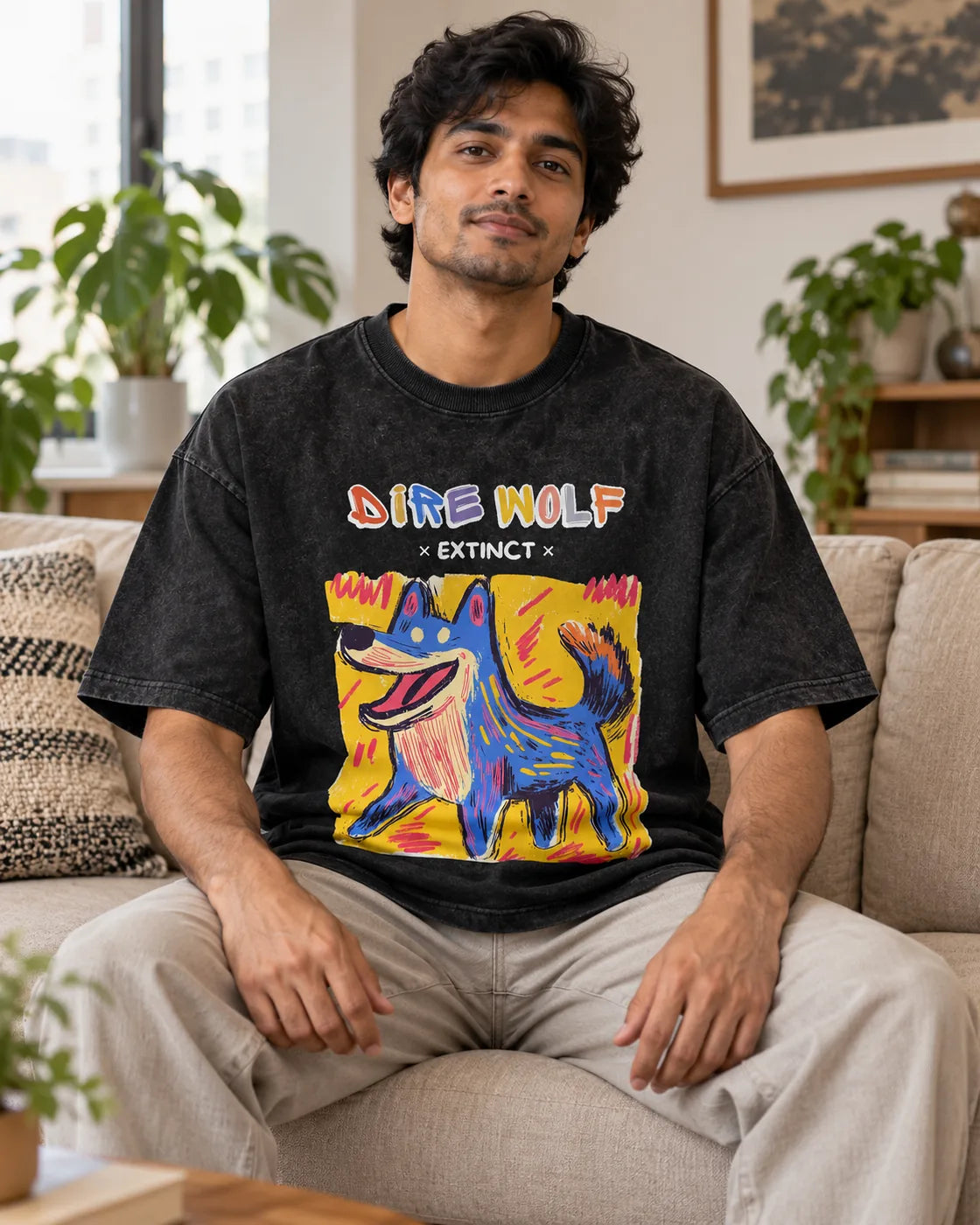 Model wearing the Dire Wolf black acid wash oversized T-shirt seated on a sofa, Fourth Dimension Club