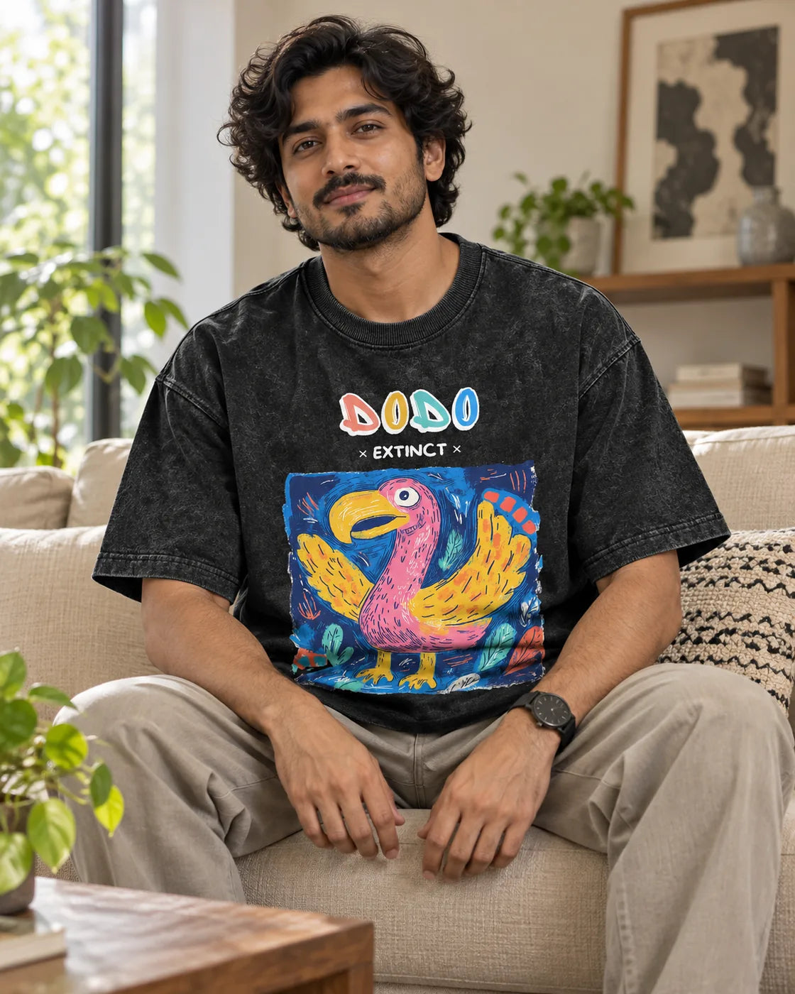 Model wearing the Dodo black acid wash oversized T-shirt seated on a sofa, Fourth Dimension Club