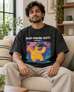 Model wearing the Giant Ground Sloth black acid wash oversized T-shirt seated on a sofa, Fourth Dimension Club