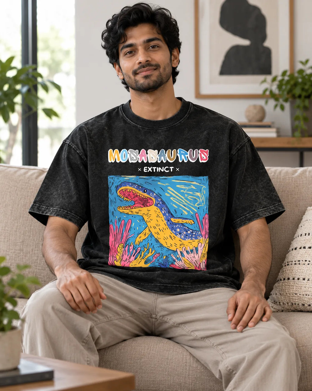 Model wearing the Mosasaurus black acid wash oversized T-shirt seated on a sofa, Fourth Dimension Club