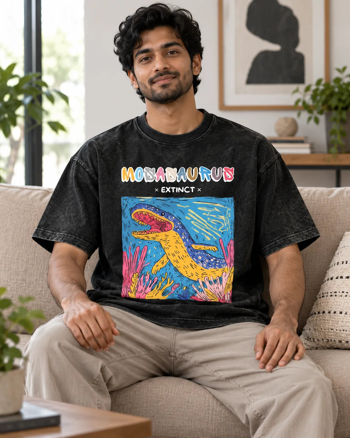 Model wearing the Mosasaurus black acid wash oversized T-shirt seated on a sofa, Fourth Dimension Club