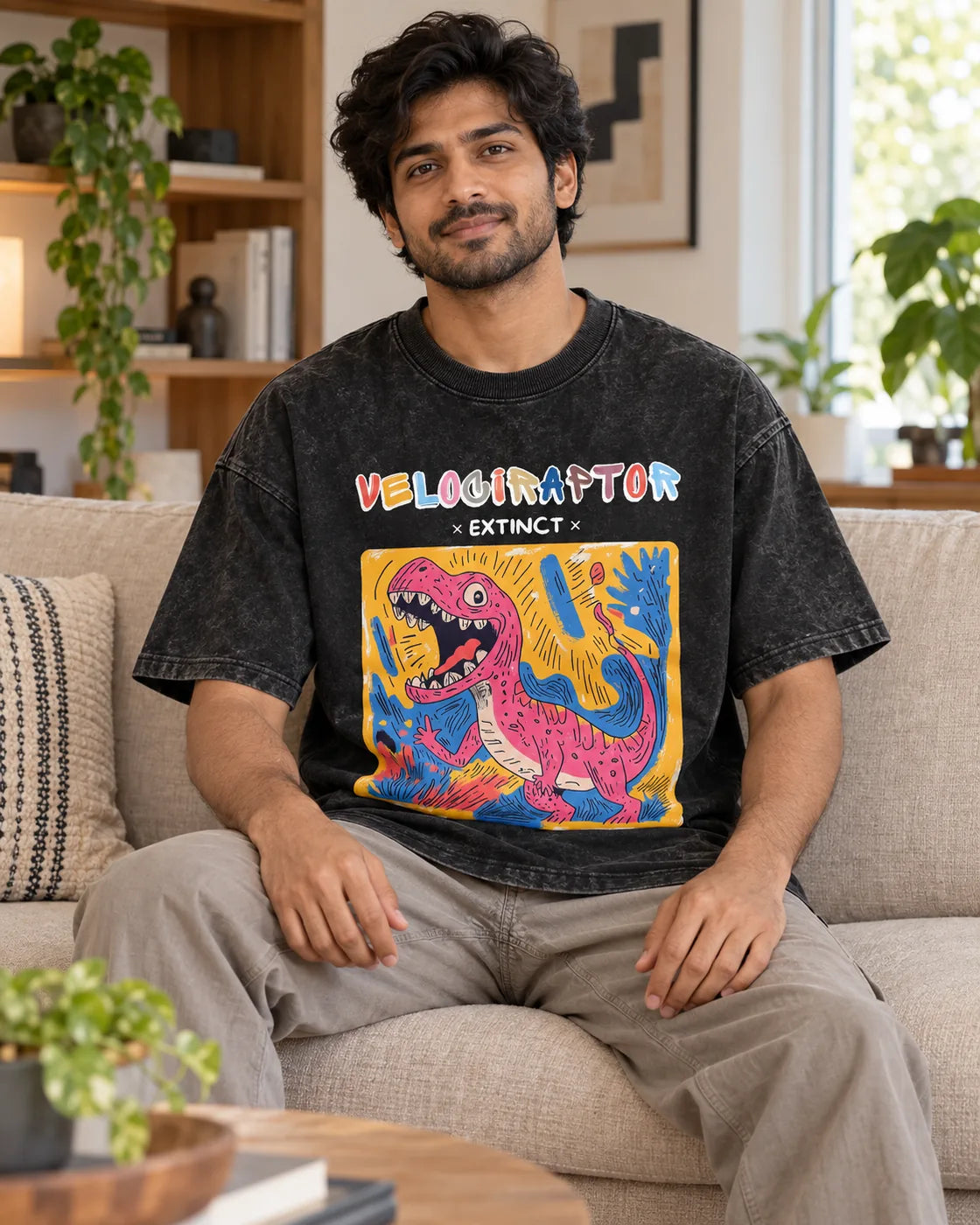 Model wearing the Velociraptor black acid wash oversized T-shirt seated on a sofa, Fourth Dimension Club