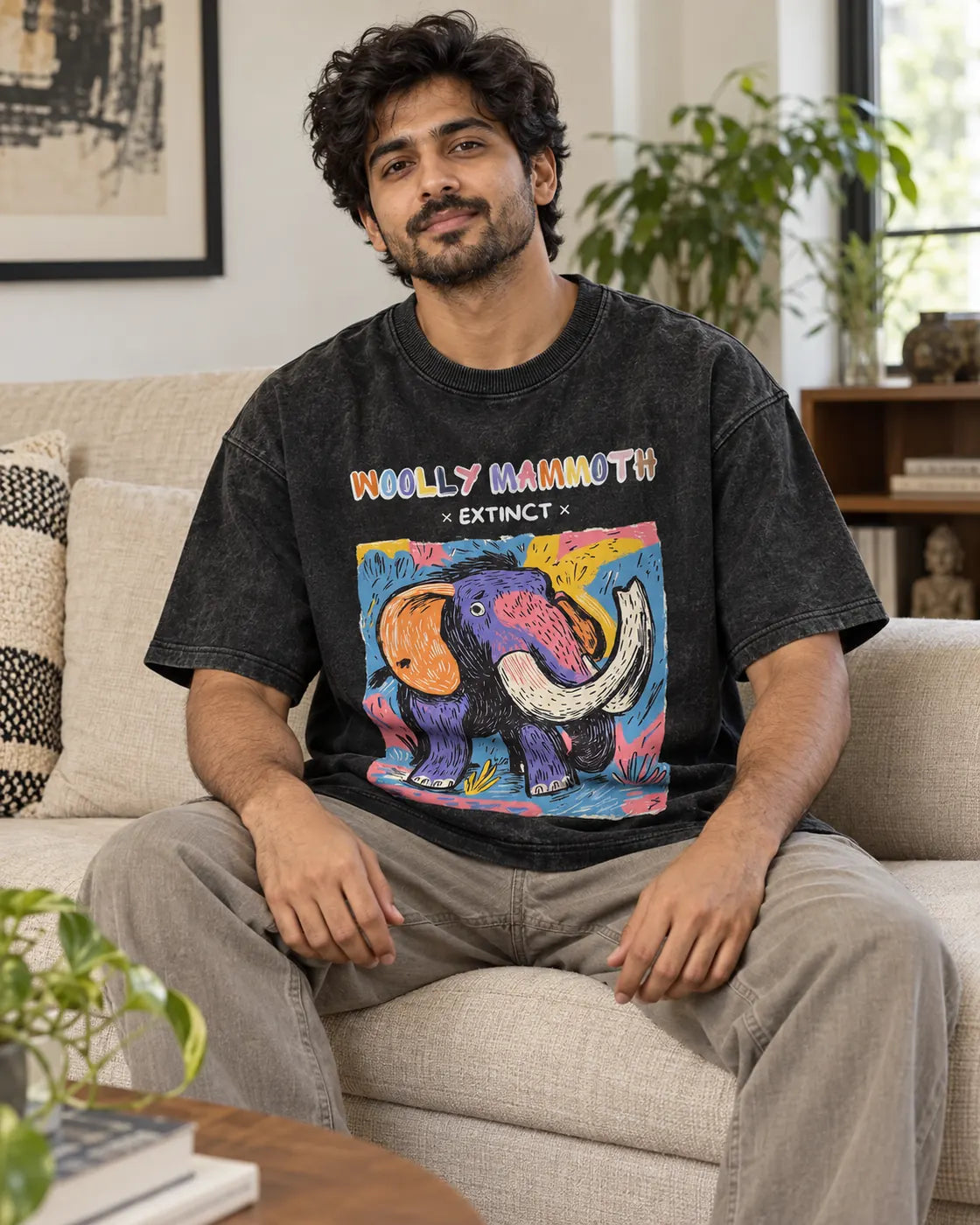 Model wearing the Woolly Mammoth black acid wash oversized T-shirt seated on a sofa, Fourth Dimension Club