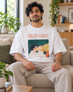 Model wearing the Edwin Hubble Genius Doodles oversized French terry T-shirt by Fourth Dimension Club, seated on a sofa