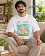 Model wearing the Jane Goodall Genius Doodles oversized French terry T-shirt by Fourth Dimension Club, seated on a sofa