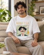 Model wearing the Nikola Tesla Genius Doodles oversized French terry T-shirt by Fourth Dimension Club, seated on a sofa