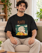 Model wearing the Plato Genius Doodles oversized French terry T-shirt by Fourth Dimension Club, seated on a sofa