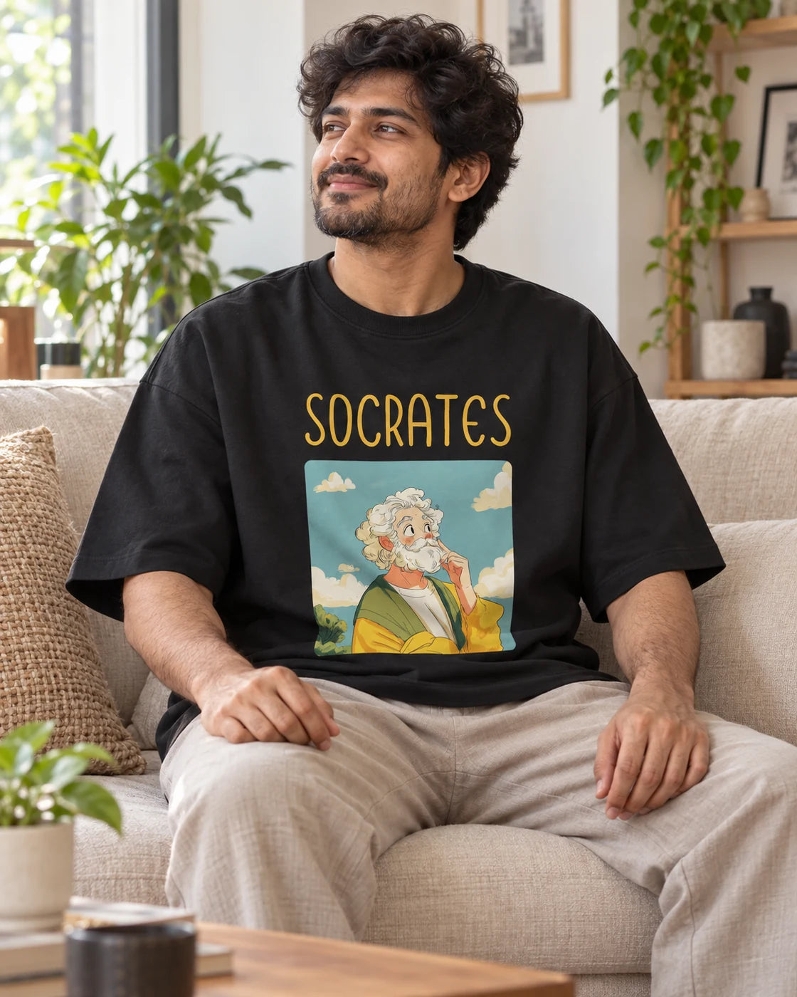 Model wearing the Socrates Genius Doodles oversized French terry T-shirt by Fourth Dimension Club, seated on a sofa