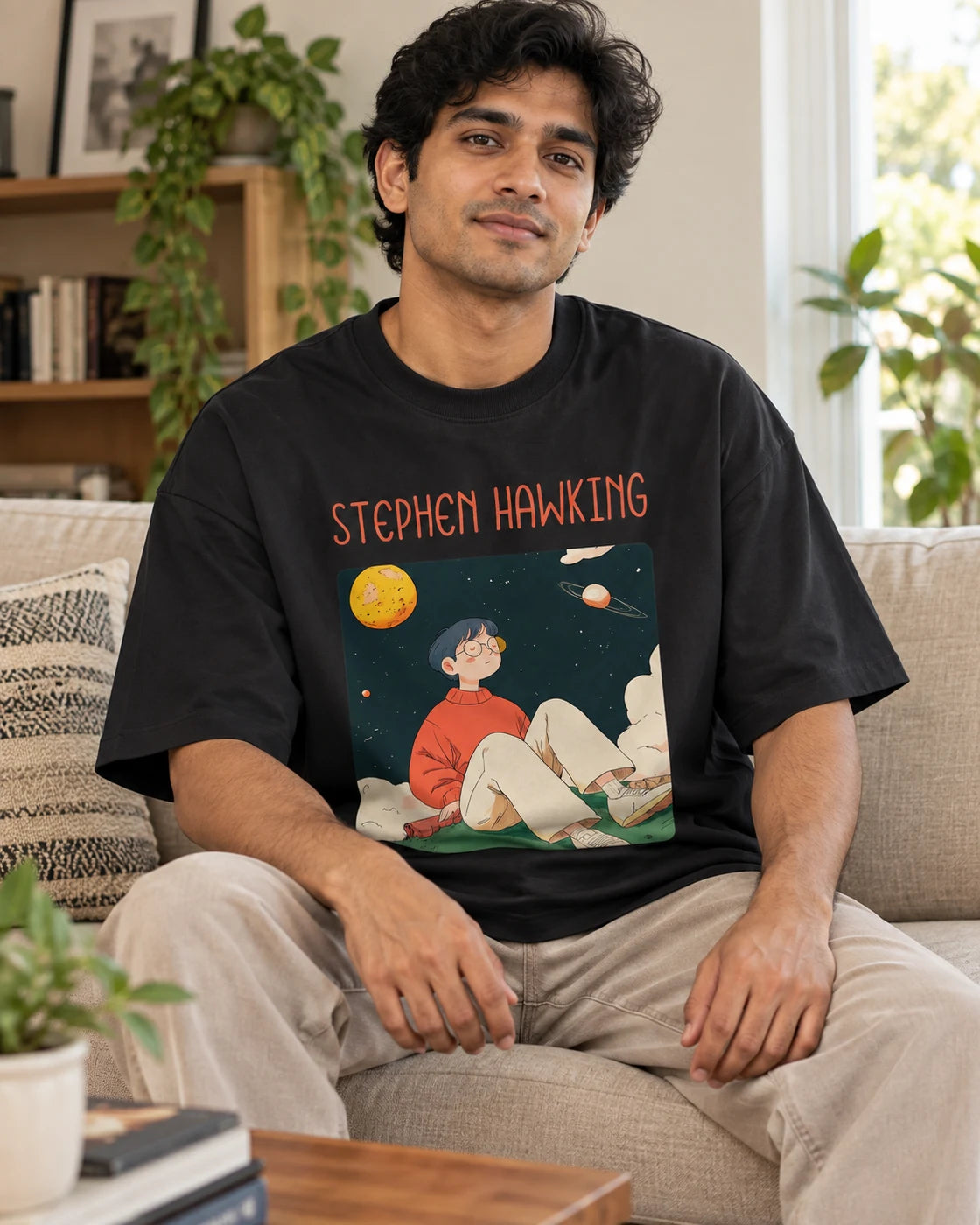 Model wearing the Stephen Hawking Genius Doodles oversized French terry T-shirt by Fourth Dimension Club, seated on a sofa