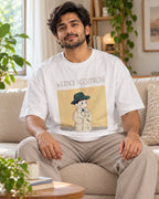 Model wearing the Werner Heisenberg Genius Doodles oversized French terry T-shirt by Fourth Dimension Club, seated on a sofa