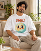 Model wearing the Venus Stellar Squad oversized French terry T-shirt in white by Fourth Dimension Club, seated on a sofa